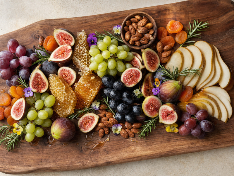 Cheese and fruit grazing board arranged with figs, honey, and almonds